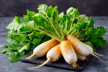 Fresh daikon radishes with green leaves resting on a dark slate boardの素材