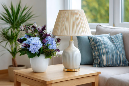 Living room interior featuring a wooden side table with flowers and a lamp next to a comfortable sofaの素材