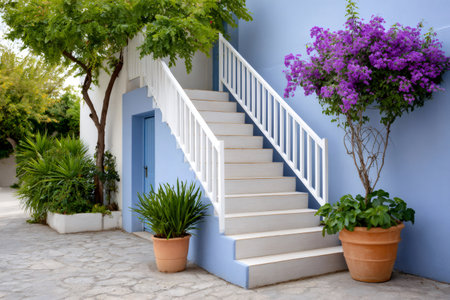 Traditional Greek building featuring blue walls, white stairs, and vibrant bougainvillea flowersの素材