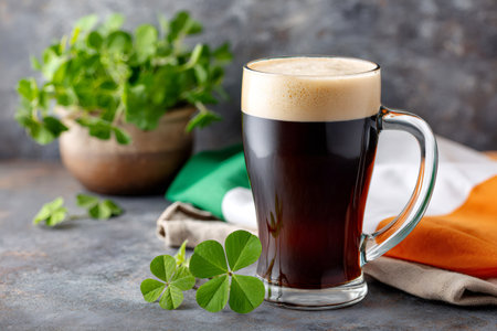 Dark stout beer in a mug with foam, shamrock leaves, and Irish flag colors for celebrationの素材