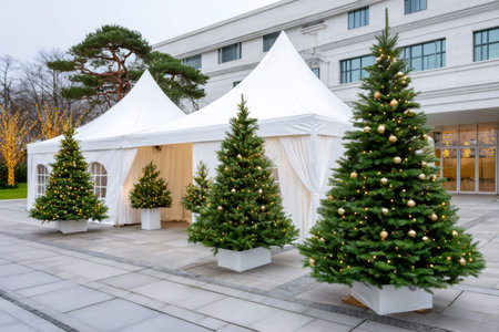 Christmas trees with gold ornaments and lights standing in front of white event marqueesの素材