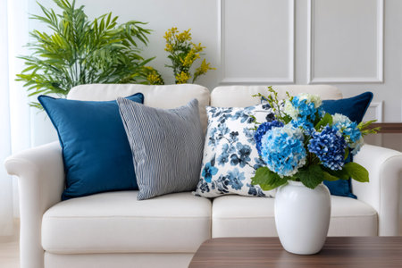 Living room sofa with decorative pillows, blue hydrangea flowers in a vase, and green plantsの素材