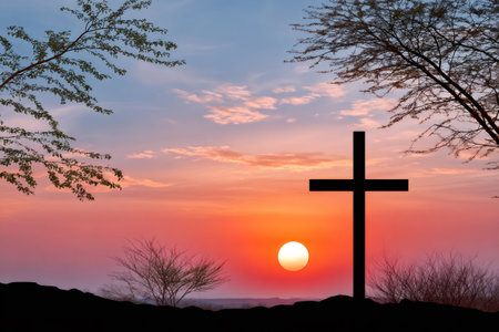 Christian cross silhouette standing on a hill watching a colorful sunsetの素材