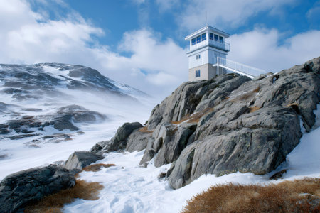 Watchtower standing on a rocky mountain slope with snow and strong wind blowing in a cold arctic landscapeの素材