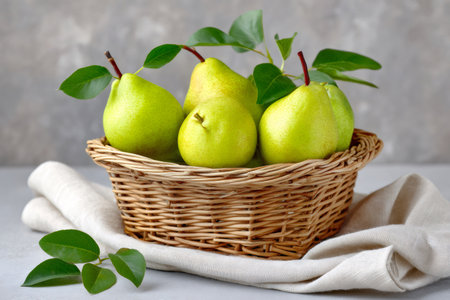 Ripe green pears with fresh leaves filling a wicker basket on a linen clothの素材