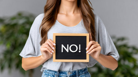 Woman holding a letter board with NO! word, symbolizing refusal and rejectionの素材