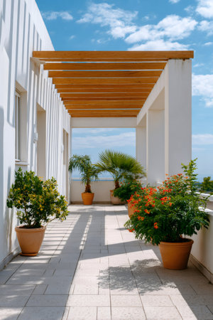 White modern house terrace featuring a wooden pergola, potted plants, and relaxing sea view on a sunny dayの素材