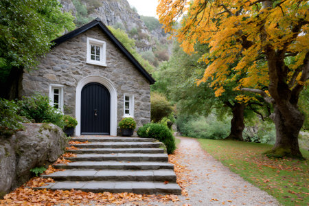 Stone cottage standing by a gravel path with autumn leaves and colorful treesの素材