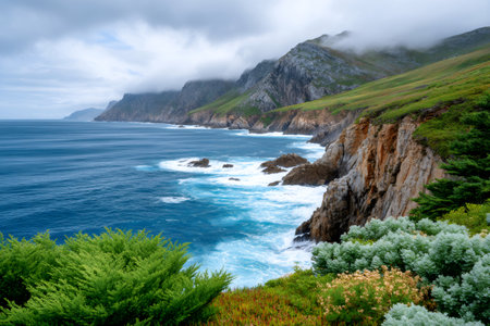 Atlantic ocean waves crashing against steep cliffs with green vegetation and fog-covered peaksの素材