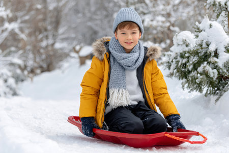 Young boy enjoying winter activities sledding down a snowy hillの素材