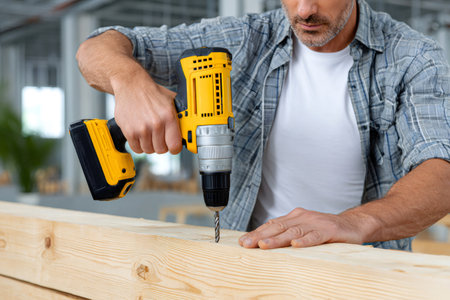 Man applying a cordless drill to create a hole in a wooden beamの素材