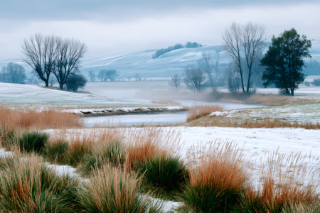 Winter season showing a peaceful frosty landscape with a meandering river and snow-dusted fieldsの素材