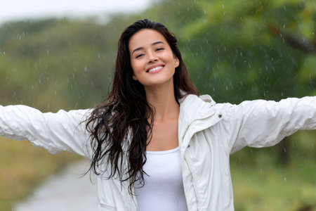 Woman smiling with arms outstretched feeling happy and free in light rainの素材