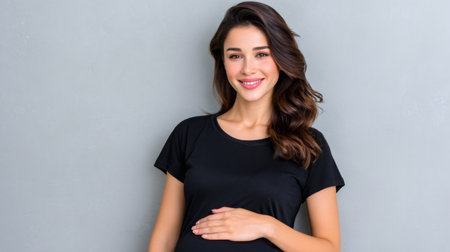 Pregnant woman smiling, looking at camera, and touching her baby bumpの素材