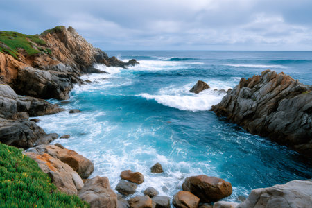 Pacific Ocean waves breaking on rugged coastal cliffs and boulders under a cloudy skyの素材
