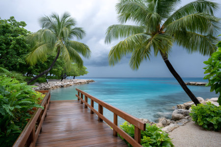 Tropical resort boardwalk extending to turquoise ocean water under a cloudy skyの素材
