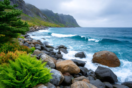 Waves crashing on a rocky coastline with green vegetation and mountains under a cloudy skyの素材