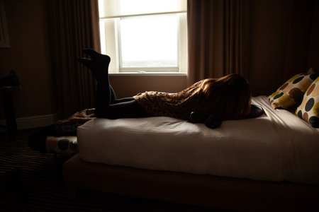 Silhouette of a young woman lying on the bed at homeの写真素材