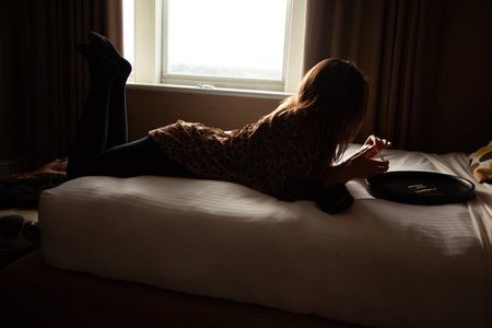 Young woman lying on the bed at home and using a mobile phoneの写真素材