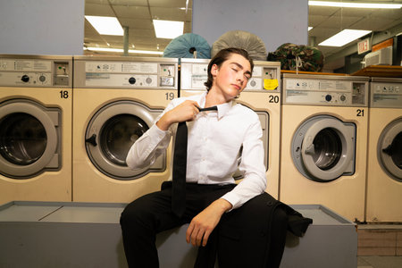 A young man in a shirt and tie in a laundromatの写真素材