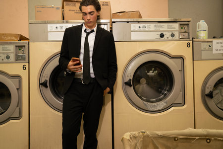 A young man in a black suit and tie with a mobile phone in a washing machineの写真素材