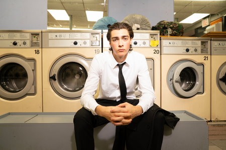 Portrait of a handsome young man sitting in front of washing machinesの写真素材
