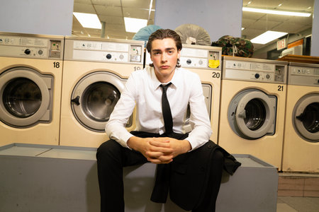 Young man sitting in front of washing machines in a laundromatの写真素材