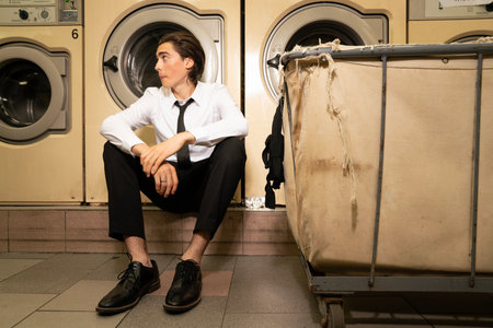 Young man sitting in front of washing machine in a laundromatの写真素材