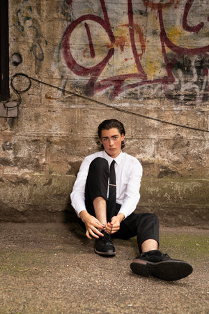 Handsome young man in white shirt and black pants sitting on the groundの写真素材