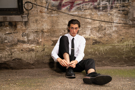 Handsome young man in a white shirt and black tie sitting on the ground.の写真素材