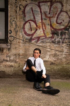 Young man sitting in front of a wall with graffiti on it.の写真素材