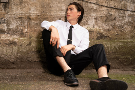 Young business man sitting on the floor in front of a stone wallの写真素材