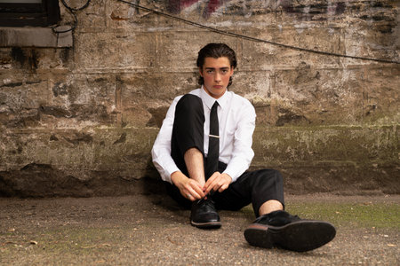 Handsome young man in white shirt and black tie sitting on the groundの写真素材