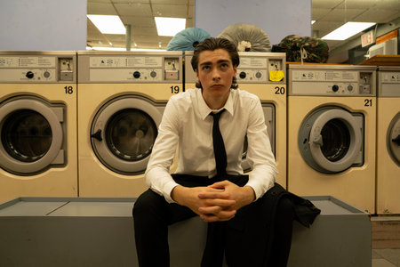 Portrait of young businessman sitting in front of washing machines in a laundromatの写真素材