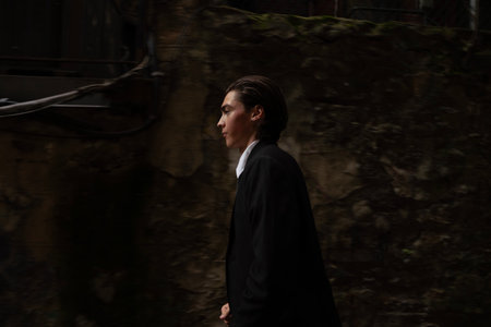 Young man in a black suit walking down the street in the cityの写真素材