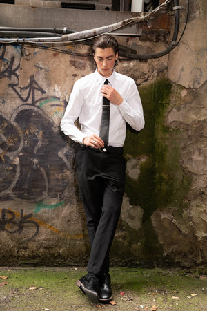 Handsome young man in a white shirt and black pants posing in an urban environmentの写真素材