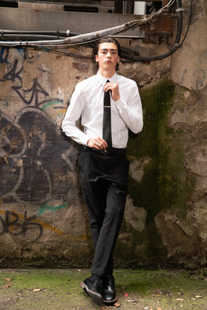 Young businessman standing in front of a graffiti wall wearing a white shirt and black pantsの写真素材