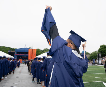 Rear view of a student in graduation robe raising his hands.の写真素材