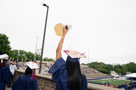 Rear view of a female graduate holding a graduation hat while standing in the crowdの写真素材