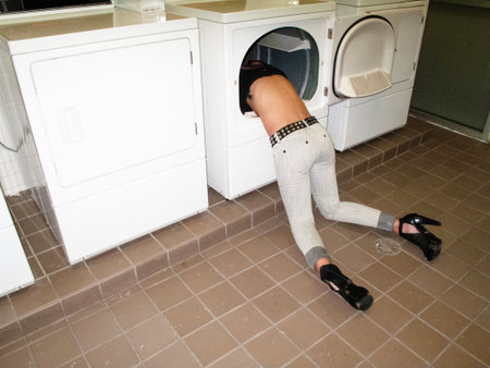 A young woman is doing laundry in a washing machine at home.の写真素材
