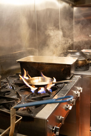 Stainless steel stove in a restaurant kitchen with fire and smokeの写真素材