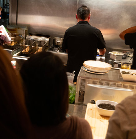 A view of a restaurant kitchen with chefs and customers in the backgroundの写真素材