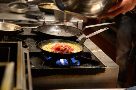 Chef cooking scrambled eggs with bacon on frying pan in restaurant kitchenの写真素材
