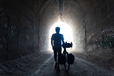 A silhouette of a man with a bicycle in a dark tunnel.の写真素材