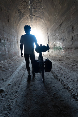 Silhouette of a man with his bicycle in a tunnel.の写真素材