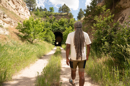 Back view of young man with dreadlocks walking through a tunnel in the woodsの写真素材