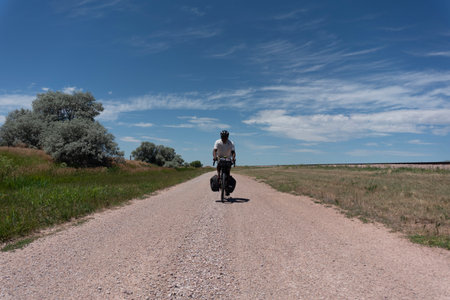Rear view of a man riding a bicycle on a country roadの写真素材