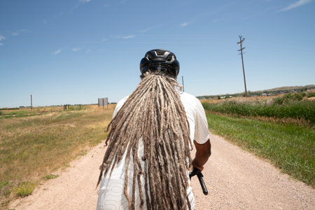 Rear view of a biker with dreadlocks standing on a dirt road