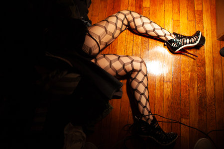 Legs of young woman in stockings and high heels on wooden floor