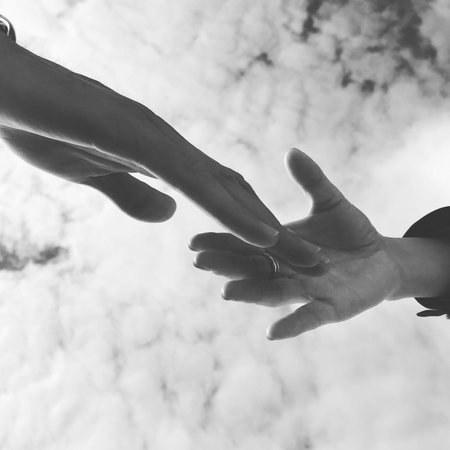 Black and white image of two hands holding each other over sky backgroundの写真素材